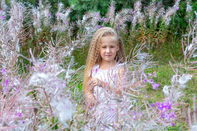 A little blonde girl in a sundress stands surrounded by blooming sally, fireweed. summer, lifestyle