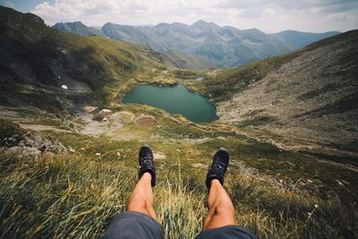 Low section of woman standing on mountain by lake against sky