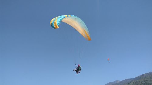 Low angle view of people paragliding against clear blue sky