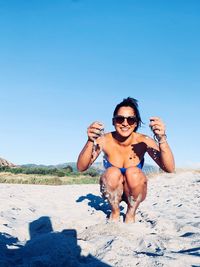 Full length of shirtless man wearing sunglasses at beach against clear sky