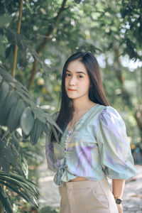 Portrait of young woman standing against trees