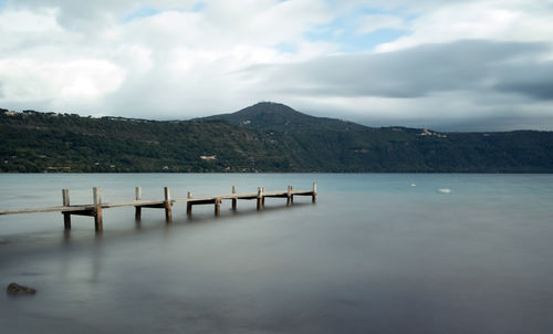 Pier on lake by mountains against sky