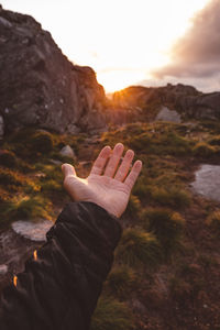 Midsection of person on rock against sky during sunset