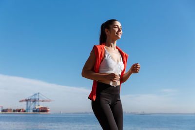Young woman jogging by sea against sky