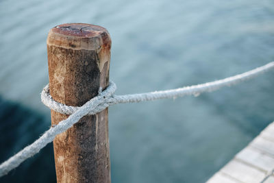 Close-up of rope tied to wooden post at harbor