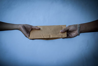 Cropped hands holding envelope against white wall