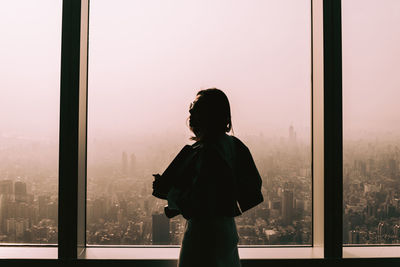 Woman standing by window against clear sky