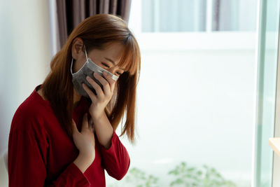 Portrait of beautiful young woman photographing against window