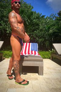 Tattooed man in thong standing by american flag on lounge chair at poolside