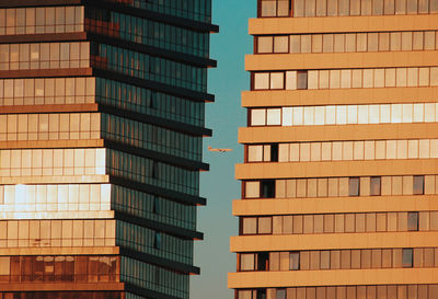 Low angle view of modern buildings in city against sky, and a plane flying through