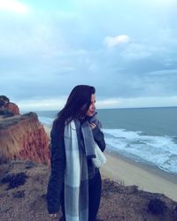 Young woman standing at beach against sky