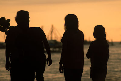 Silhouette friends standing against sea during sunset