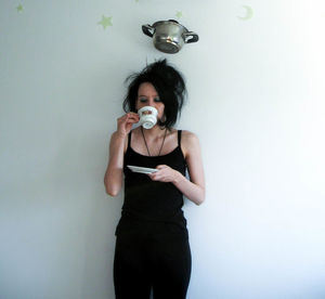 Cooking pan over woman drinking cup and saucer against wall at home