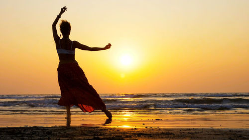 Man with arms raised on beach during sunset