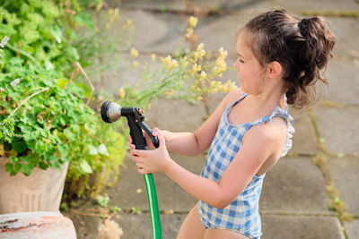 Young girl is watering plants in the backyard while wearing a bathing suit