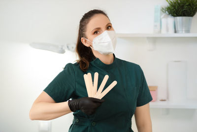 Portrait of young woman wearing protective mask while standing against wall