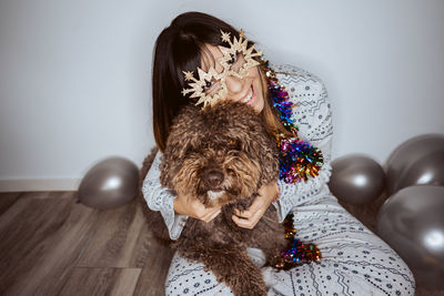 Smiling woman wearing mask sitting with dog and balloons on floor at home