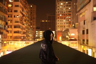 Rear view of man standing on street amidst buildings in city at night