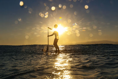 Silhouette woman standing in sea against sky during sunset