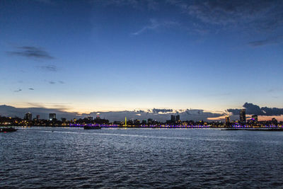 Sea by buildings against sky during sunset in city