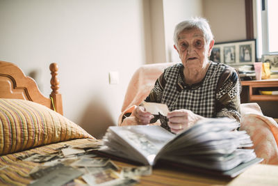 Portrait of senior woman adding old photos to a photo album at home