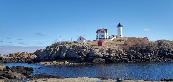 Lighthouse by sea against buildings against clear blue sky