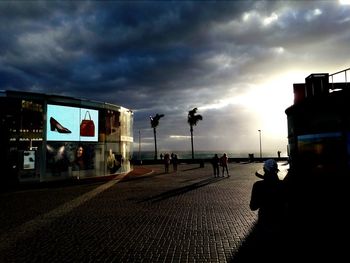 Silhouette people walking in illuminated city against sky