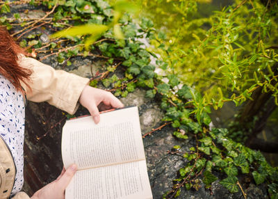 Midsection of woman reading book by plants