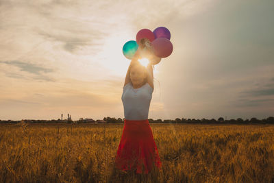 Full length of woman holding balloons on field against sky