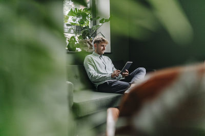 Young man sitting on green couch, using digital tablet