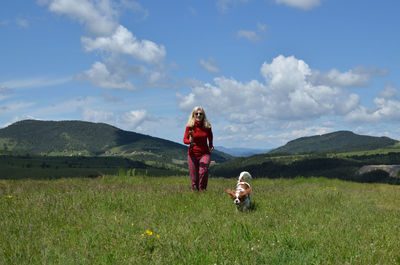 Woman dressed in red and her dog cavalier king charles spaniel running on a mountain meadow