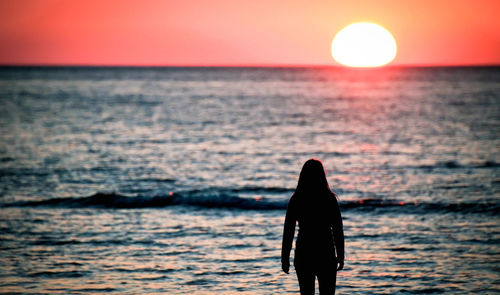 Silhouette woman standing in sea against sky during sunset