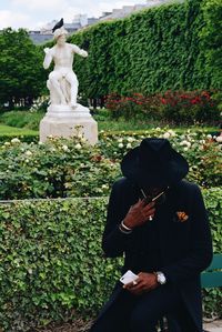 Man sitting by statue in garden