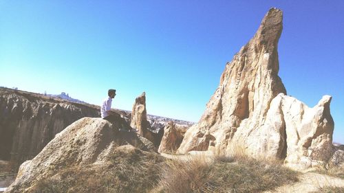 Man sitting on rock at cappadocia against clear sky