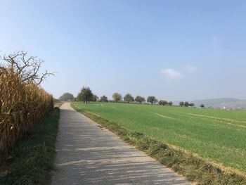 Dirt road amidst field against sky