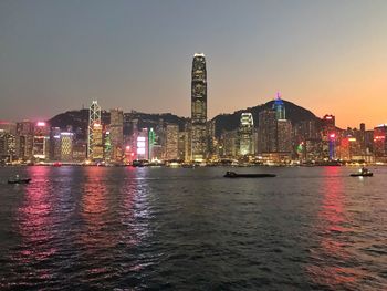 Illuminated buildings by river against sky at night