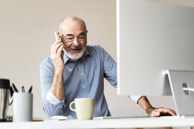 Senior freelancer talking on smart phone at desk