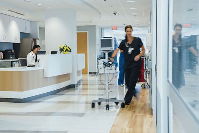 Female doctor working at reception while nurse taking monitoring equipment at hospital