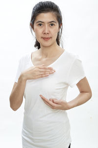 Portrait of woman touching breast against white background