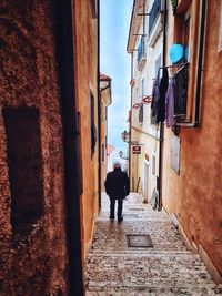 Rear view of man walking on narrow alley amidst buildings