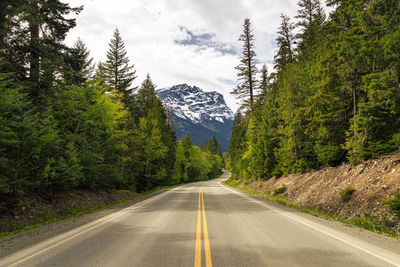 Road amidst trees and mountains against sky