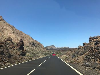 Road leading towards mountain against clear blue sky