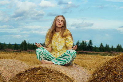 Young man sitting on field against sky