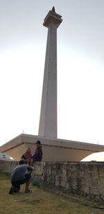 Low angle view of people sitting on column against sky