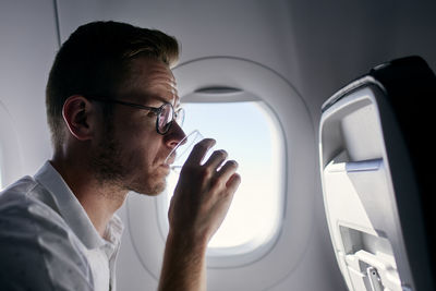 Portrait of passenger during flight. young man drinking water from plastic cup.