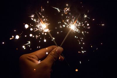 Cropped hand of person holding illuminated sparklers at night