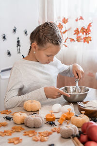 Cute little girl whips ginger dough to make cookies for halloween in the home kitchen