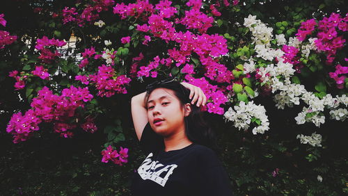 Portrait of beautiful young woman with pink flower standing against plants