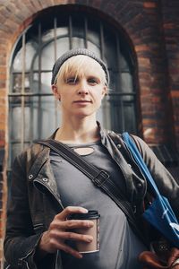 Portrait of young woman holding camera while standing outdoors