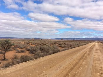 Dirt road amidst field against sky